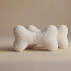 Two plush bone-shaped pet toys in a soft off-white faux fur material, arranged on a neutral beige background.