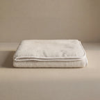 A folded cashmere cream blanket with a stitched border, displayed on a matching beige surface against a neutral beige background.