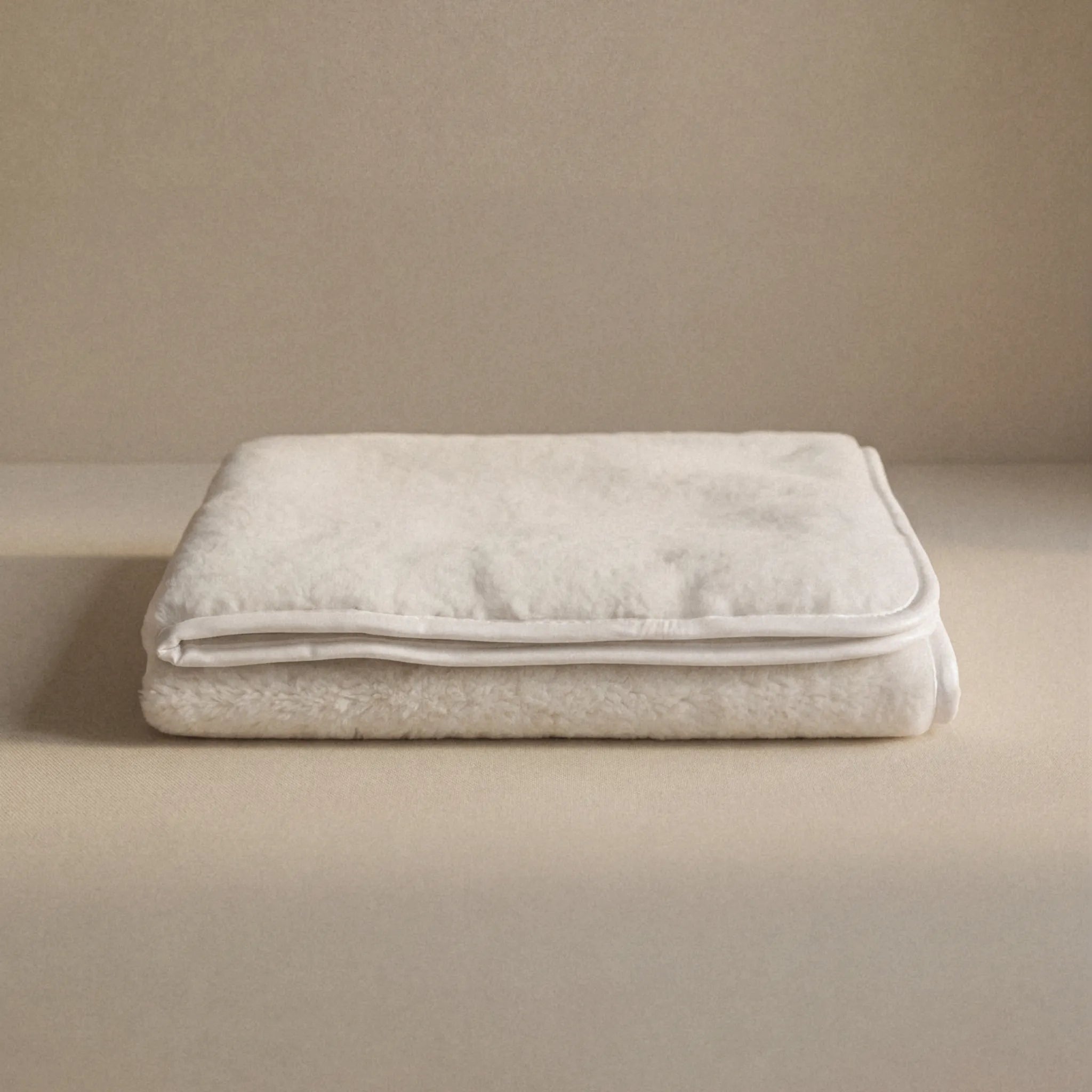 A folded cashmere cream blanket with a stitched border, displayed on a matching beige surface against a neutral beige background.