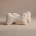 Two textured wool bone-shaped pet pillows in an off-white bouclé wool fabric, displayed on a neutral beige background.