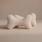 Two textured wool bone-shaped pet pillows in an off-white bouclé wool fabric, displayed on a neutral beige background.