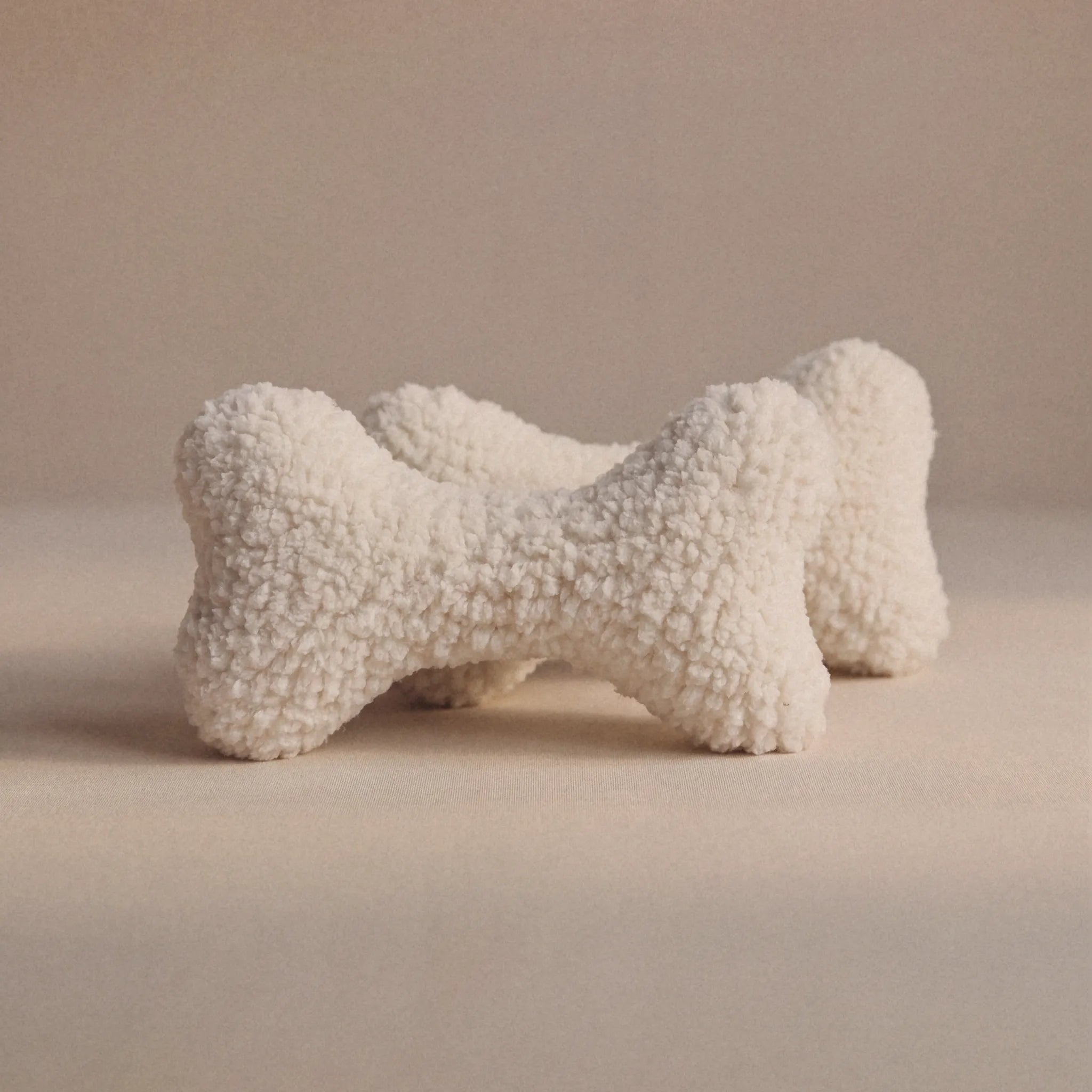 Two textured wool bone-shaped pet pillows in an off-white bouclé wool fabric, displayed on a neutral beige background.