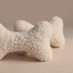 Two textured wool bone-shaped pet pillows in an off-white bouclé wool fabric, displayed on a neutral beige background.