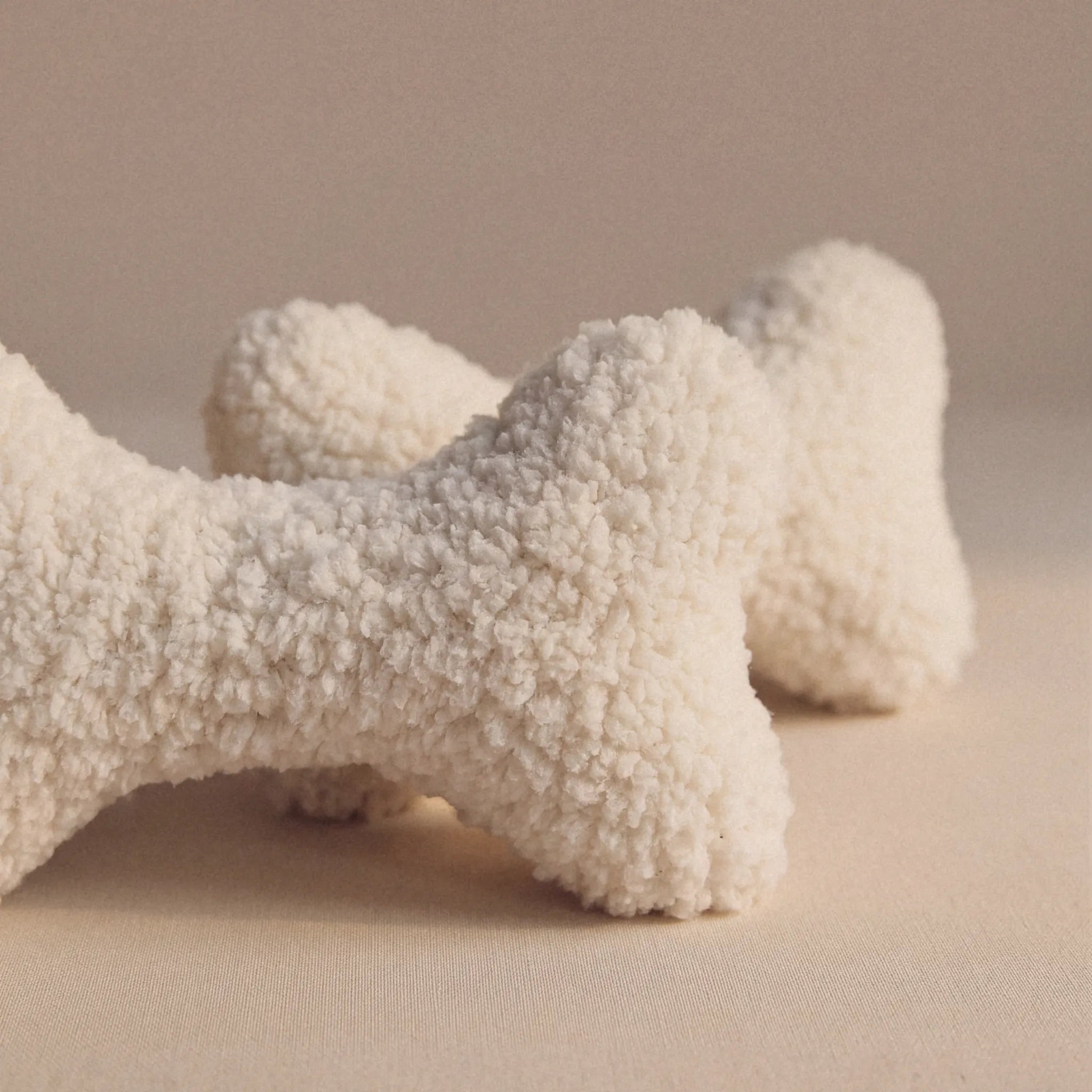 Two textured wool bone-shaped pet pillows in an off-white bouclé wool fabric, displayed on a neutral beige background.