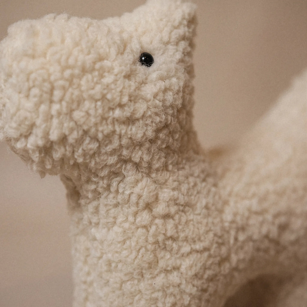 Close-up of a small wool plush pet toy featuring a bouclé loop textured material, standing on a neutral beige background.