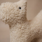 Close-up of a small wool plush pet toy featuring a bouclé loop textured material, standing on a neutral beige background.
