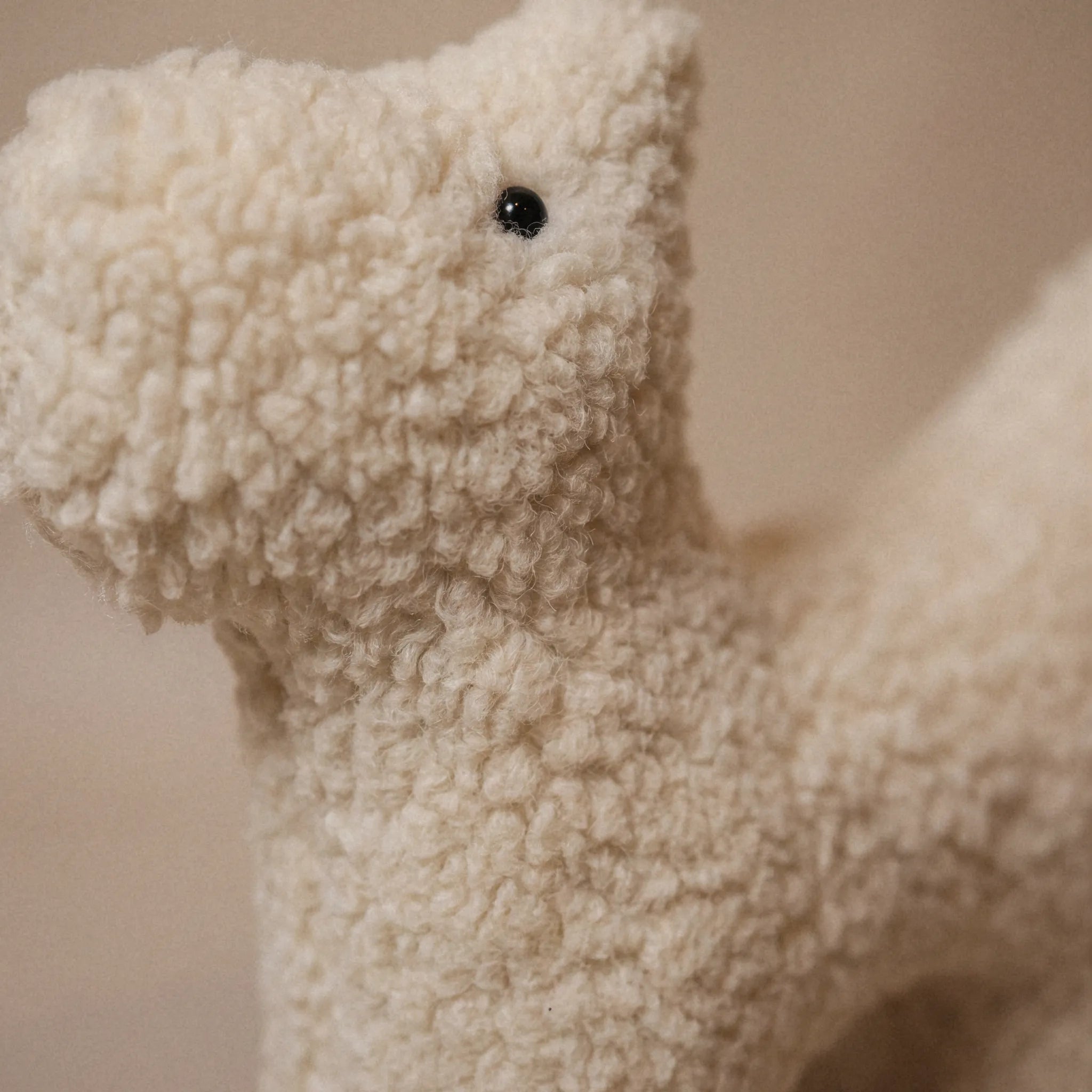 Close-up of a small wool plush pet toy featuring a bouclé loop textured material, standing on a neutral beige background.