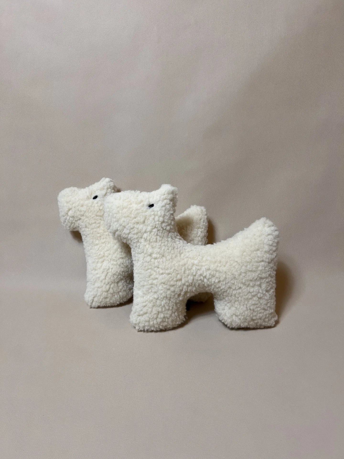Two small wool plush pet toys featuring a bouclé loop textured material, standing on a neutral beige background.