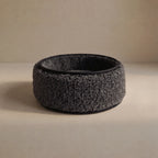 A dark wool sheep bouclé pet bed, with a black interior and base, photographed on a neutral beige surface and background.