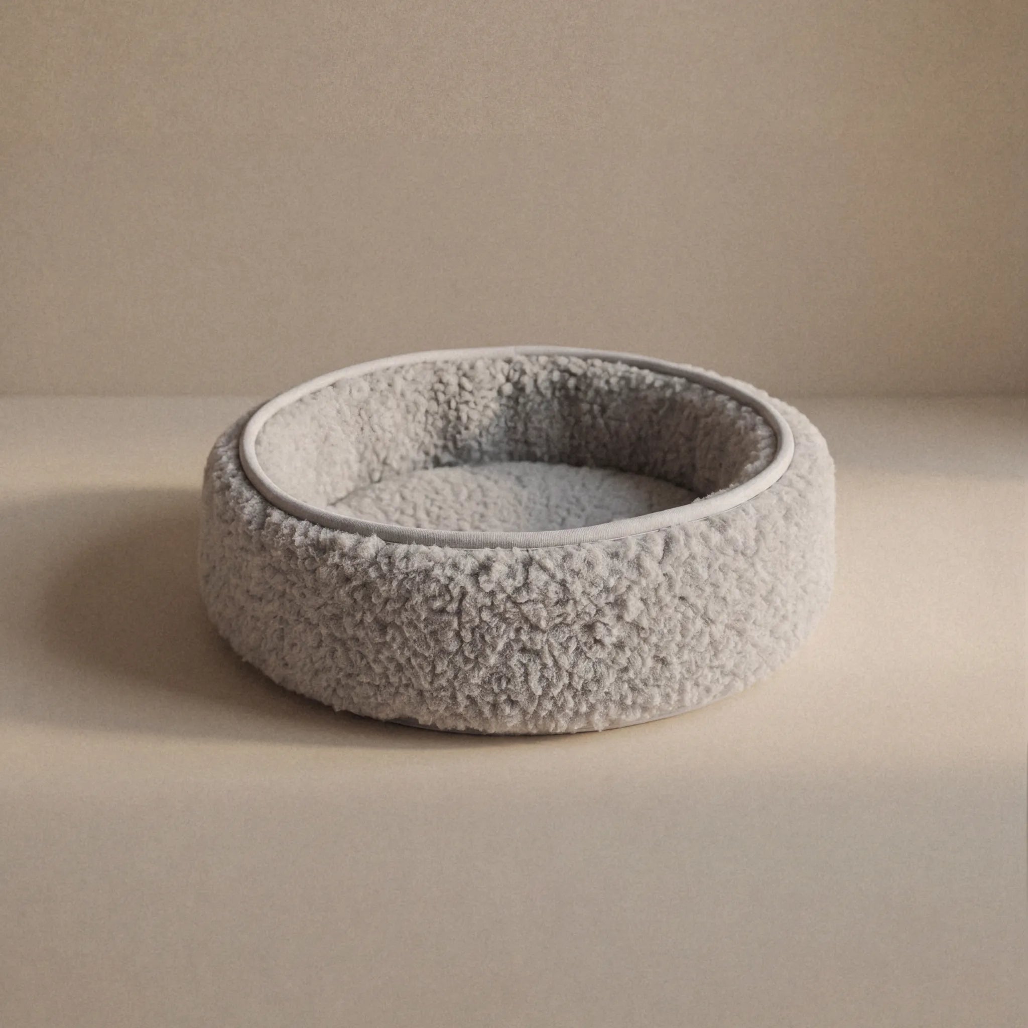 A round, wool sheep bouclé pet bed, with a textured, wool exterior and a soft, cushioned interior, shown on a neutral beige background.