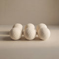 Six off-white wool balls arranged in two rows on a neutral beige surface against a matching beige background.