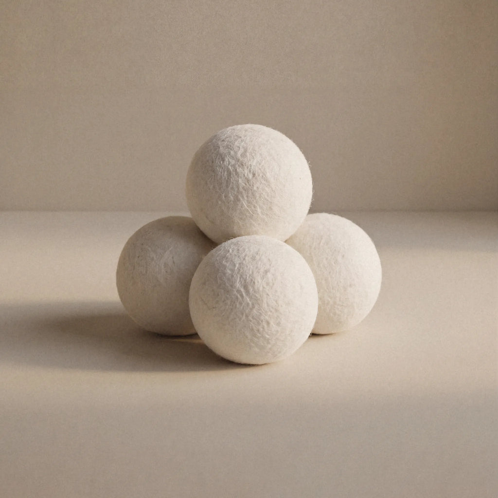 Four textured white wool balls arranged in a pyramid on a warm beige surface against a matching beige background.