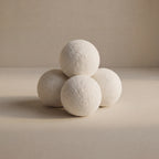 Four textured white wool balls arranged in a pyramid on a warm beige surface against a matching beige background.