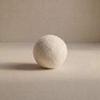 A single off-white wool ball, standing upright on a neutral beige surface against a matching beige background.