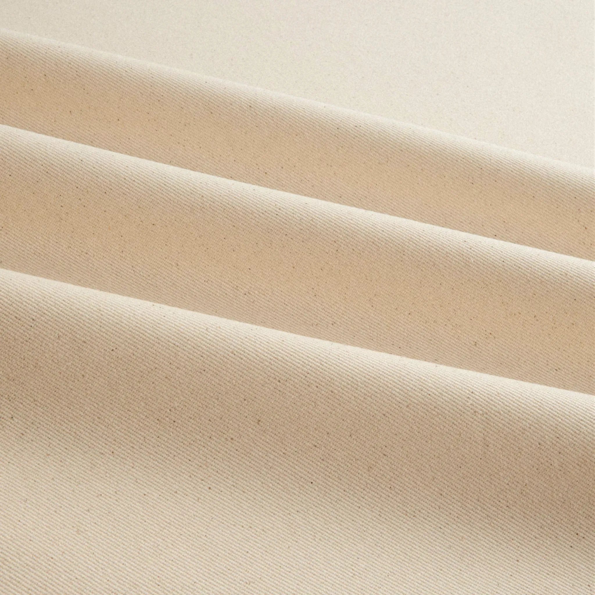 A close-up of cotton canvas fabric in beige colour with a fine woven texture and subtle speckling, arranged in soft diagonal folds.