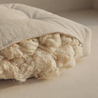 A close-up of a cotton cushion showing its thick, wool filling and a light beige fabric cover.