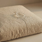 A close-up of a beige pet bed with water droplets and a small water splash on its surface, demonstrating a water-resistant or waterproof finish.