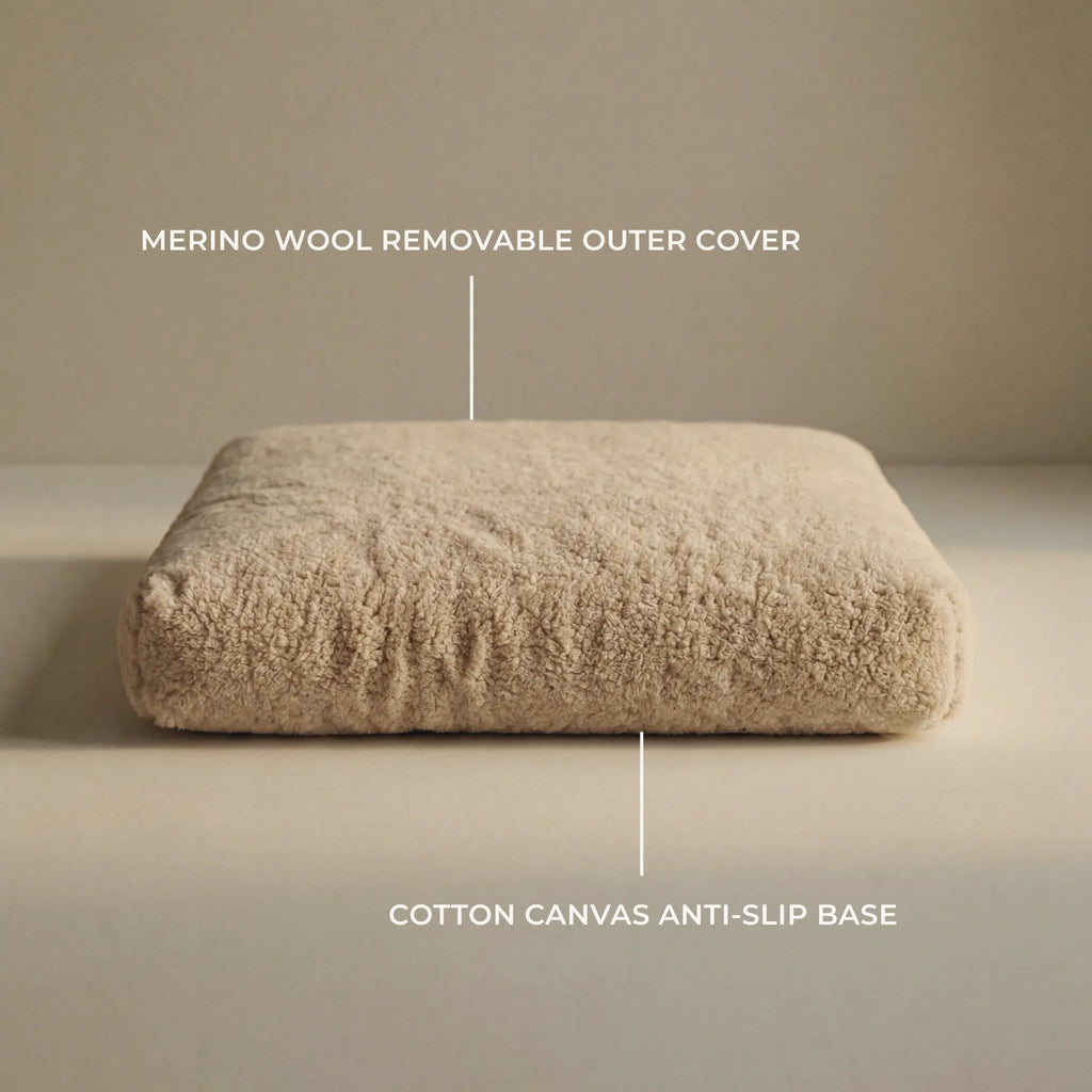 A rectangular beige 'Wool Lounge Bouclé Pet Bed' on a plain beige studio background, with overlaid text labels pointing to a merino wool removable outer cover and a cotton canvas anti-slip base.
