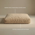 A rectangular beige 'Wool Lounge Bouclé Pet Bed' on a plain beige studio background, with overlaid text labels pointing to a merino wool removable outer cover and a cotton canvas anti-slip base.